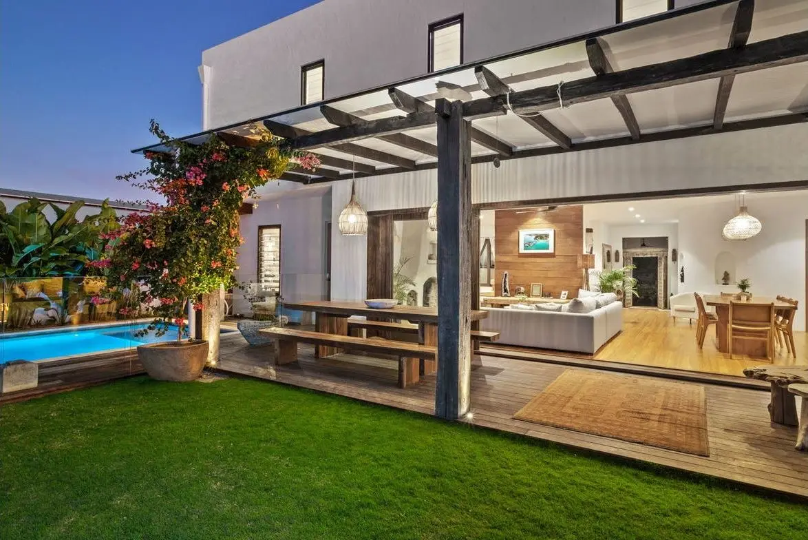 Covered alfresco opening to the lawn and pool at dusk